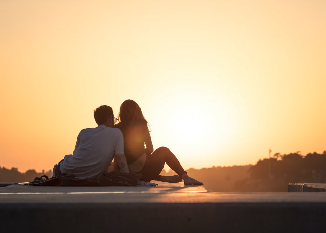 Paar sitzt eng umschlungen bei Sonnenuntergang mit Blick auf die Landschaft.